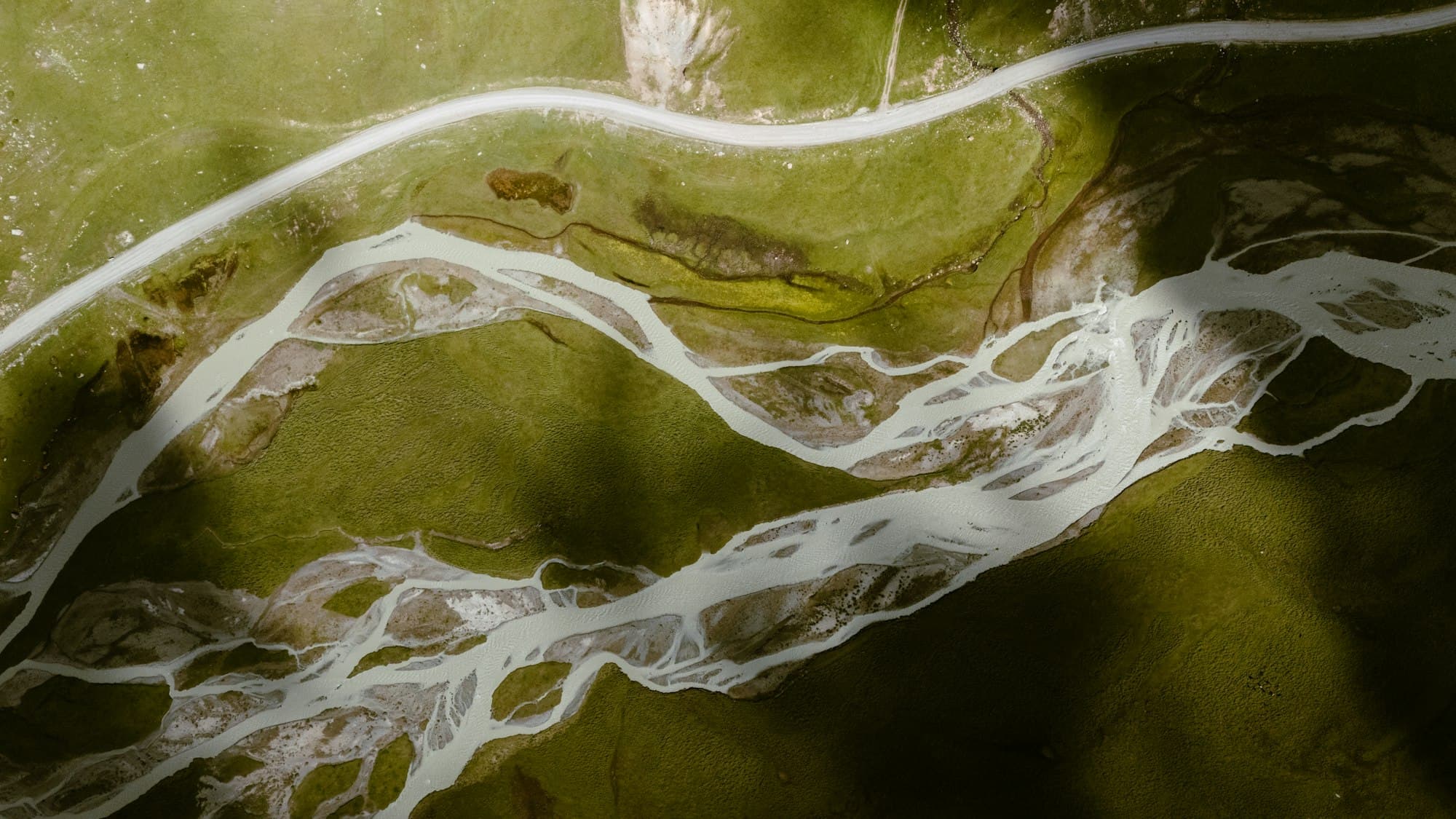 A braided river seen from above, one stream splitting into dozens of pale channels across dark green land