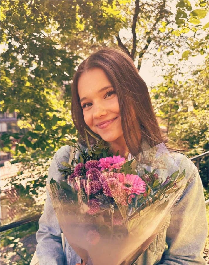 Ciara holding a bouquet of pink and purple flowers, smiling in the sunshine